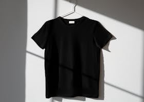 Minimalist image of a black t-shirt on a hanger with dramatic shadows on a white wall.